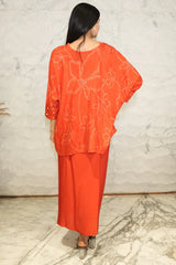 بلوزة فضفاضة بأكمام واسعة من قماش الموسلين الخالص المطبوع بنقشة بانداني حمراء من موش، مع تنورة دائرية ملفوفة من حرير المودال الأحمر مزودة بإبزيم.